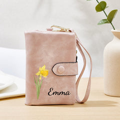 Personalized blush pink wallet with wrist strap, featuring a custom name 'Emma' in elegant script and a delicate yellow daffodil floral design. Stylish and functional, this custom gift is perfect for women who love unique and meaningful accessories.